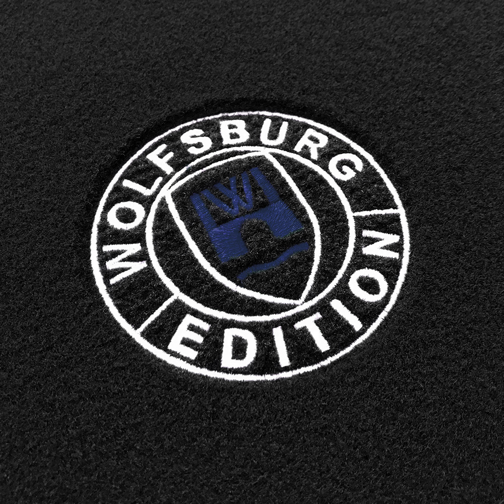 Das gestickte Wolfsburg Editions Logo auf einem schwarzen Teppich und das Logo ist in dunkelblau.