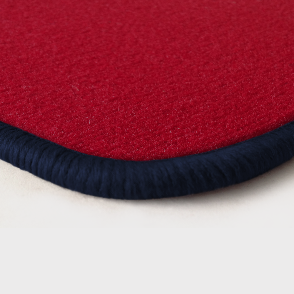 Eine Ecke als Beispiel einer Fussmatte Velours rot mit Rand in dunkelblau.