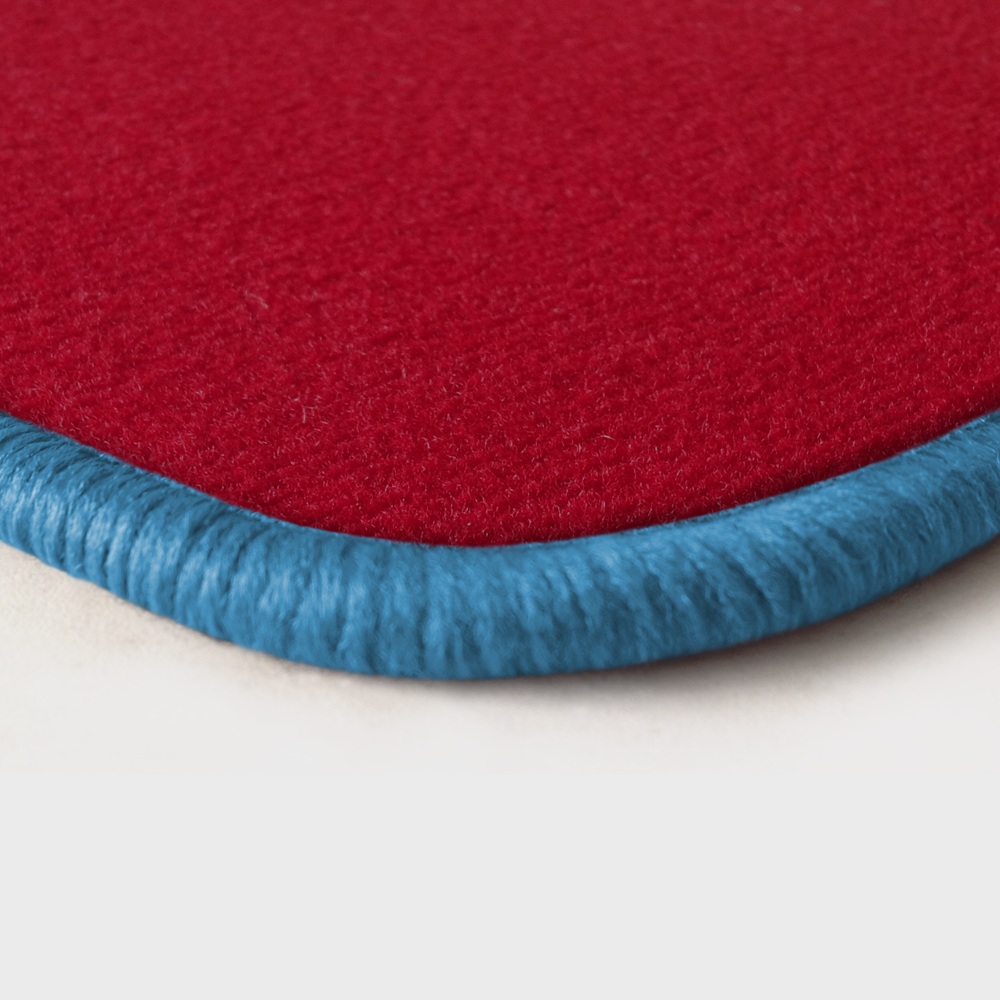 Eine Ecke als Beispiel einer Fussmatte Velours rot mit Rand in hellblau.