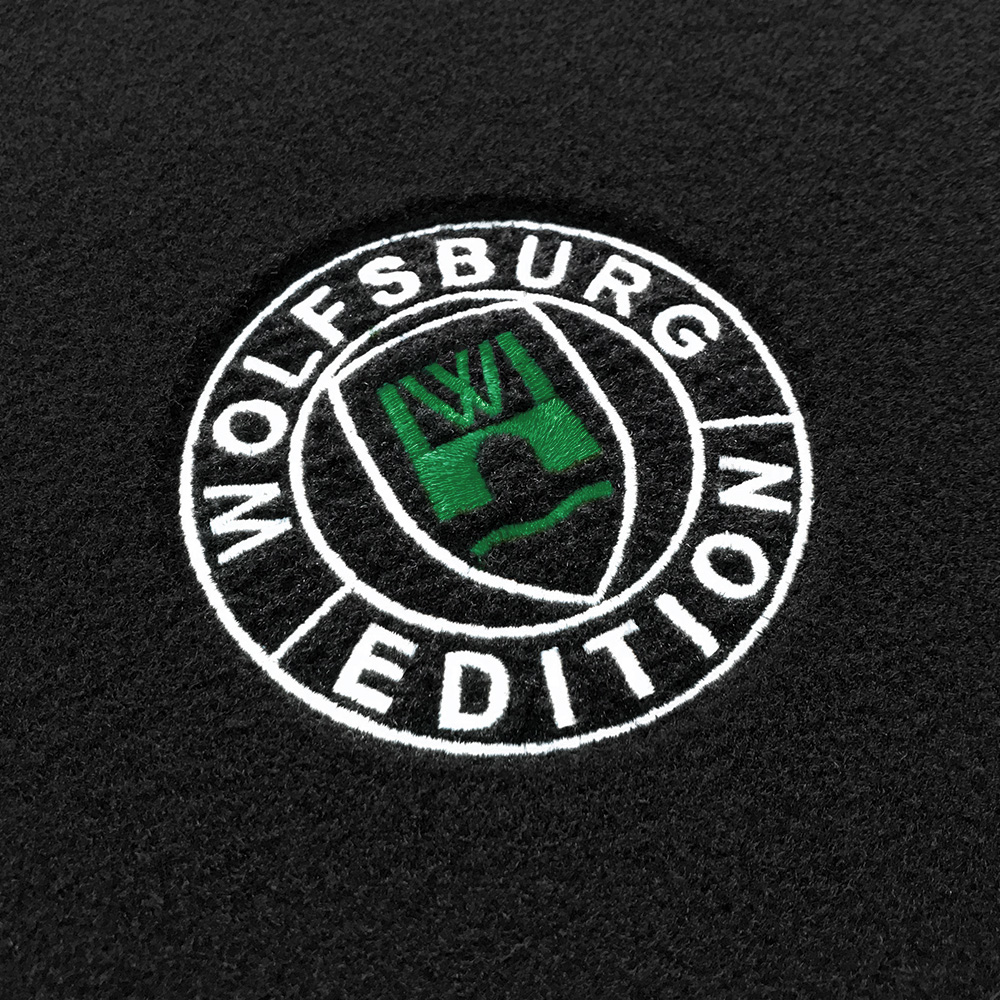 Das gestickte Wolfsburg Editions Logo auf einem schwarzen Teppich und das Logo ist in dunkelgruen.